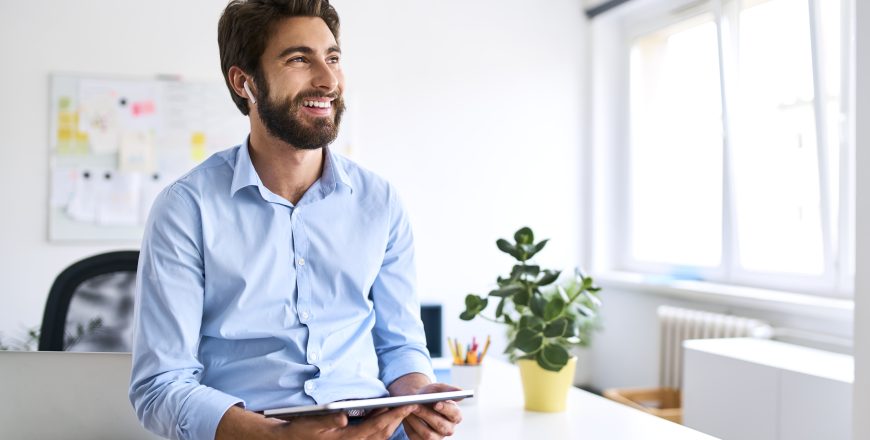 Smiling businessman with headphones using a digital tablet in his office