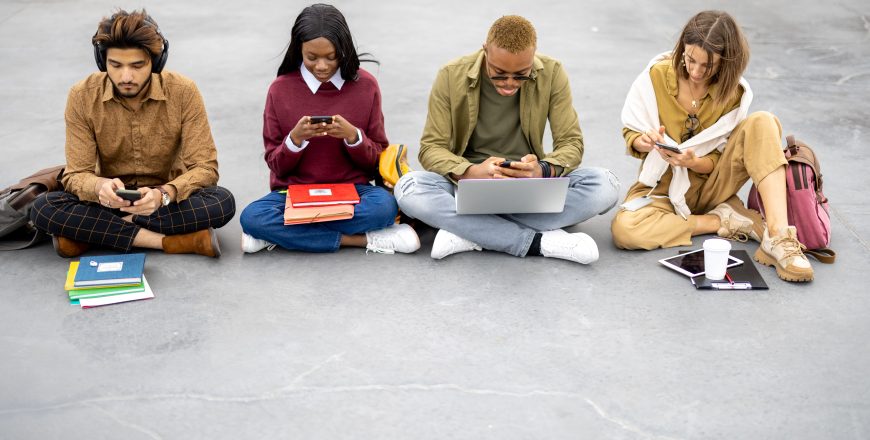 Students with digital devices sitting on asphalt